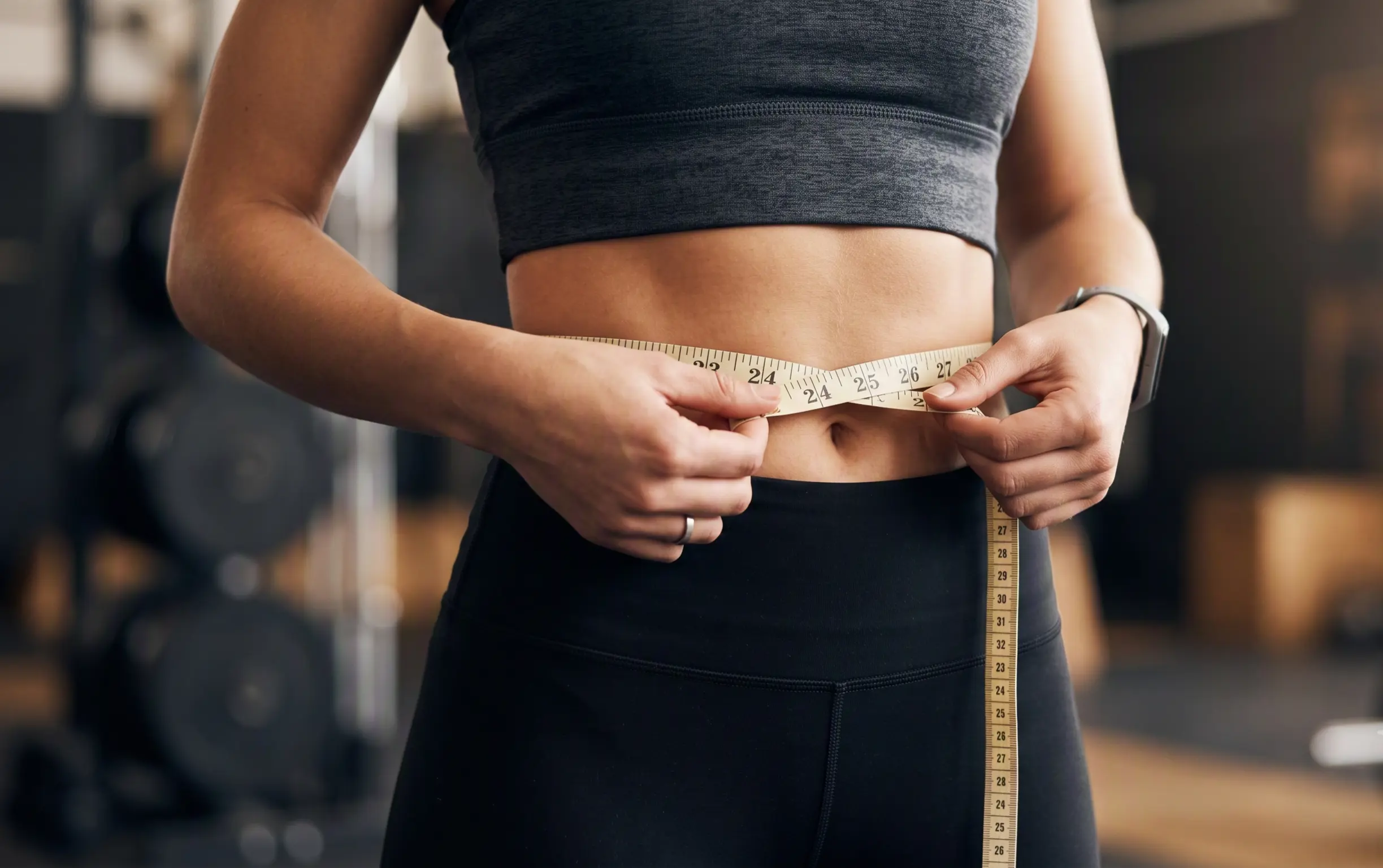 A woman measuring her waist with a tape measure at the gym